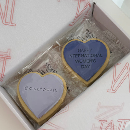 Two heart-shaped cookies in a box with 'Happy International Women's Day' text, branded 'GIVETOGAIN'.